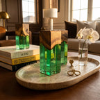 Three rectangular candle holders featuring a natural wood top section and a translucent green resin base. The holders are arranged on an oval travertine tray alongside a clear glass vase containing a white orchid and gold wick trimmers.