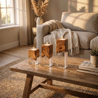 Three square candle holders of varying heights, each featuring a natural brown wood top section with a live edge and a clear, transparent acrylic base. Each holder contains a small, lit white tea light candle on the top surface.