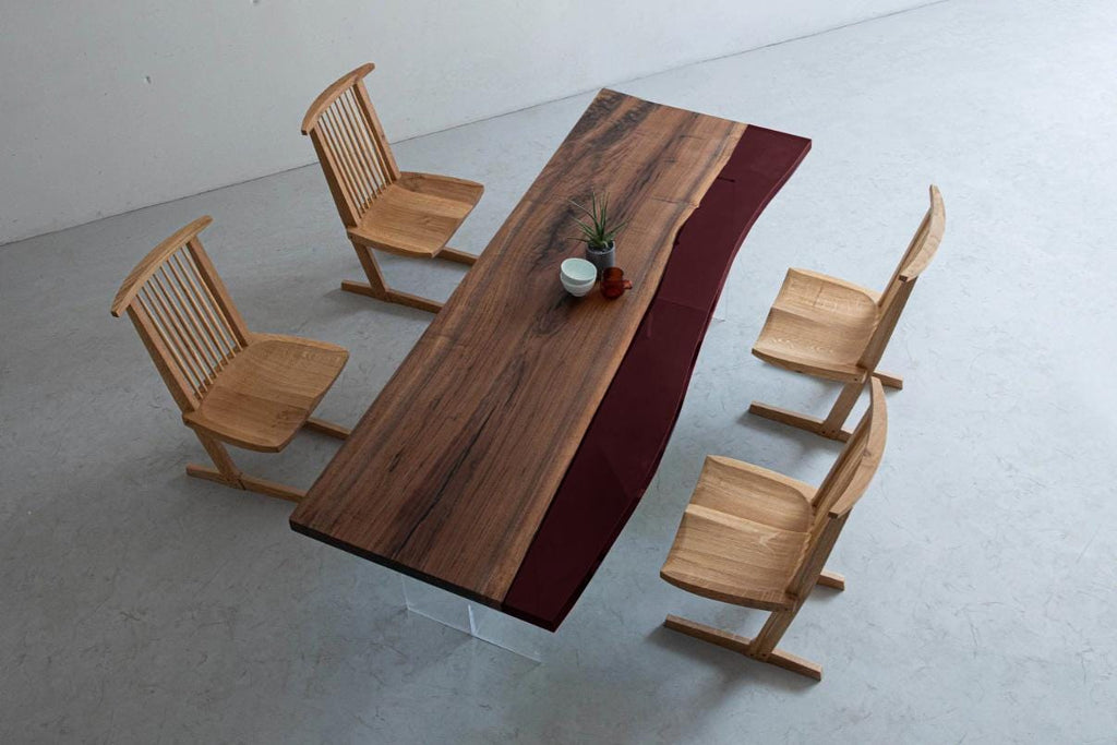 A dining set featuring a long rectangular table with a natural wood grain top, a deep red resin section, and clear acrylic legs, accompanied by four light-colored wooden chairs with spindle backs and angled support bases.