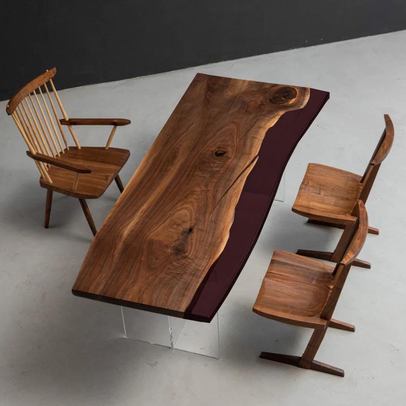 A rectangular dining table with a natural live-edge walnut wood top and a deep burgundy resin inlay, supported by clear acrylic legs. The set includes one spindle-back chair and two angular wooden chairs with solid seats and backrests.