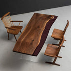 A rectangular dining table with a natural live-edge walnut wood top and a deep burgundy resin inlay, supported by clear acrylic legs. The set includes one spindle-back chair and two angular wooden chairs with solid seats and backrests.