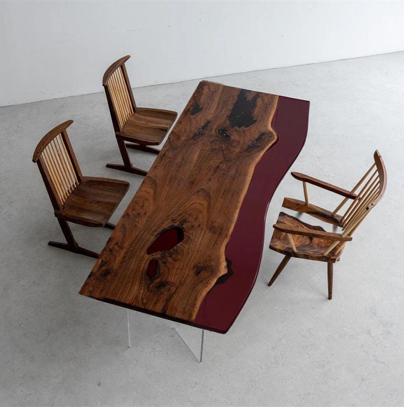 A rectangular dining table featuring a live-edge wood slab with a dark red resin inlay and clear acrylic legs, accompanied by three wooden chairs with vertical slat backrests and angled frames, arranged in a high-angle view.