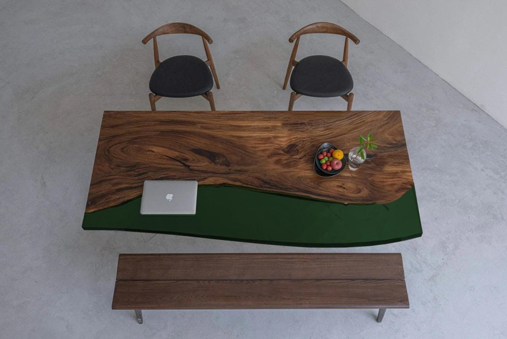 A rectangular dining table featuring a natural live-edge wood slab paired with a solid dark green resin section. The set includes two wooden chairs with black circular seats and a matching wooden bench positioned below the table.
