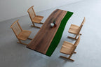 A dining set featuring a long rectangular table with a natural wood grain surface and a solid dark green resin edge, supported by clear acrylic legs, accompanied by four light-colored wooden chairs with slatted backrests.
