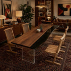 A long dining table featuring a live-edge walnut wood slab paired with a smooth black resin section, supported by clear acrylic slab legs. Four light-toned wooden chairs with vertical slat backs are arranged around the table.