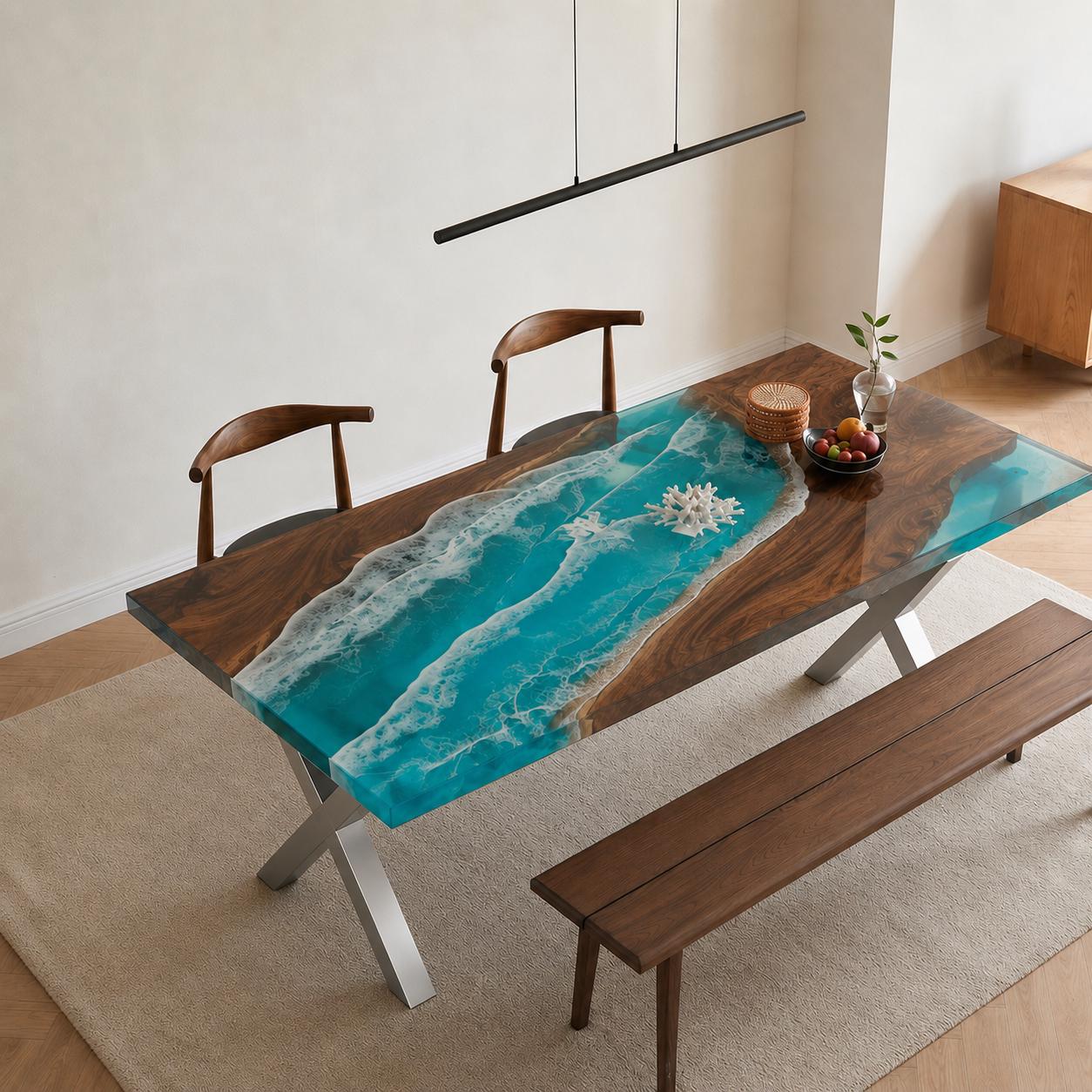 A rectangular dining table featuring a live-edge dark wood slab with a central river design made of turquoise resin that mimics ocean waves with white foam details. The table has silver-colored metal X-shaped legs and a matching bench.