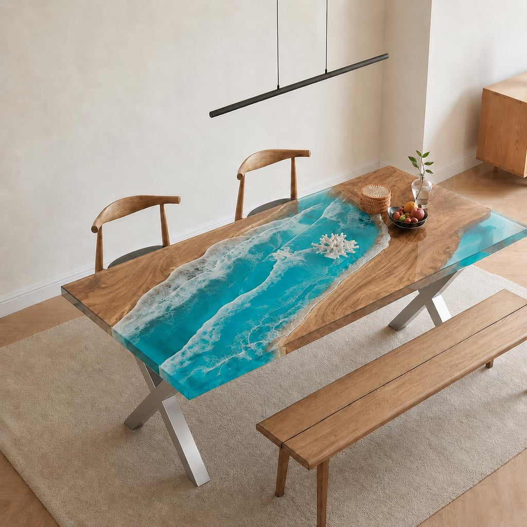 A rectangular dining table featuring a natural wood slab with a central river design made of bright turquoise resin that mimics ocean waves with white foam accents. The table has silver metal X-shaped legs and is paired with wooden chairs.