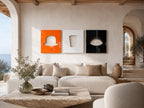 Three square wall art panels displayed in a row. The left panel is bright orange with a cutout of a bowler hat. The center panel is white with a trapezoidal cutout. The right panel is black with a cutout of an eye with eyelashes.