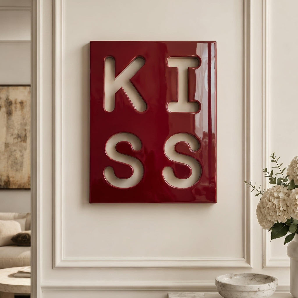 A rectangular wall art piece with a glossy deep red finish featuring the word KISS cut out in a two-by-two grid layout. The letters are arranged with K and I on the top row and S and S on the bottom row, revealing the wall behind.