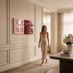 Two square wall art pieces featuring the word KISS in raised lettering. One piece is light pink and the other is deep red. The art is displayed on a paneled wall in a room with a beige slip dress, a marble table, and white flowers.