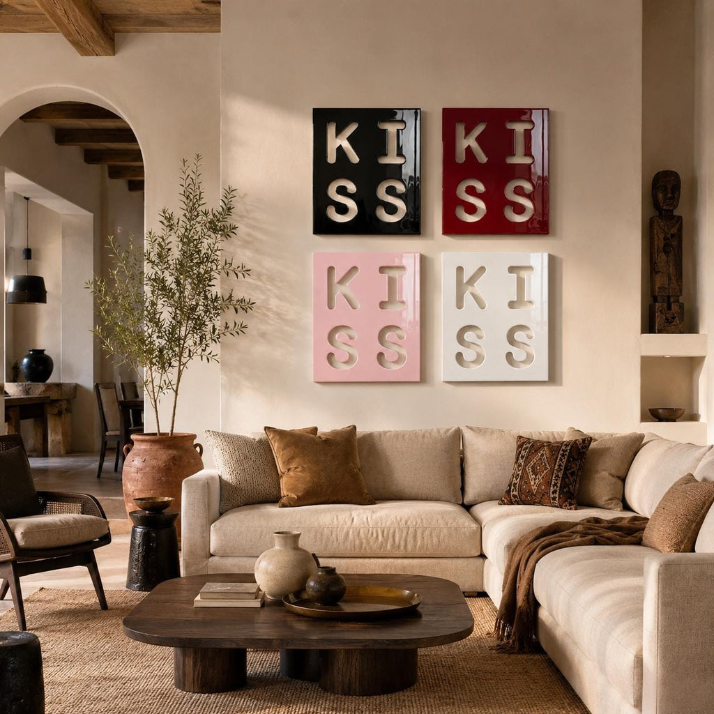 Four square wall art panels arranged in a grid, each featuring the word KISS in a bold, cut-out style. The top left panel is black, the top right is red, the bottom left is light pink, and the bottom right is white, all with glossy finishes.