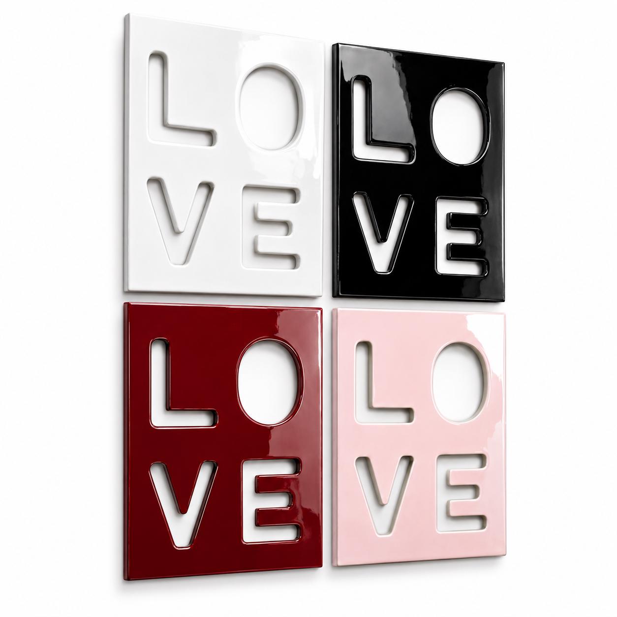 Four square wall art panels arranged in a grid, each featuring the word LOVE cut out in a block letter style. The panels are finished in glossy white, black, deep red, and light pink, creating a high-contrast display of typography.