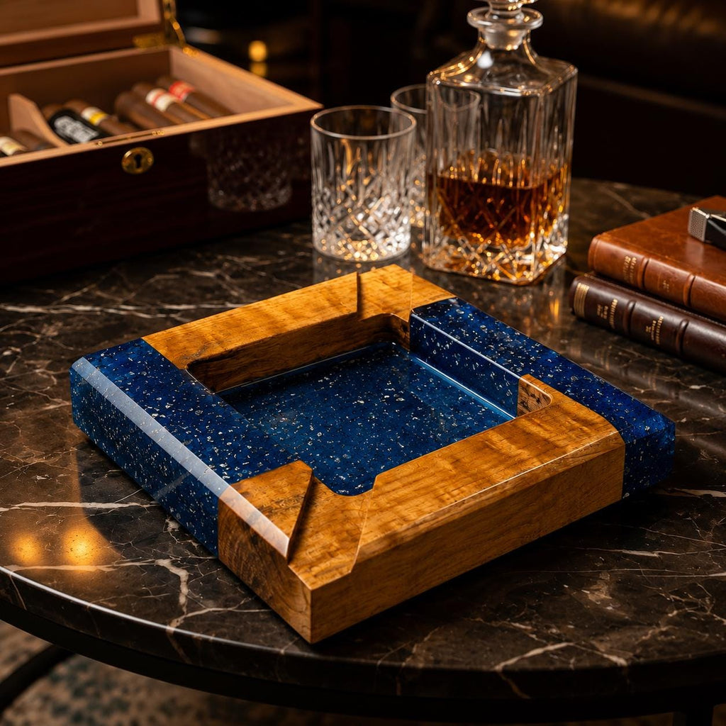 A square ashtray constructed from natural wood and deep blue resin with embedded metallic flecks. The design features four distinct corners with integrated notches for resting items, showcasing a smooth, polished finish throughout.