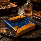 A square ashtray constructed from natural wood and deep blue resin with embedded metallic flecks. The design features four distinct corners with integrated notches for resting items, showcasing a smooth, polished finish throughout.