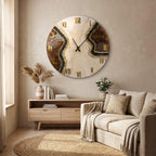 A circular wall clock featuring a marbled cream and brown resin surface with gold-colored Roman numerals. The design includes a textured black glittery vein running diagonally across the face, complemented by thin black metal clock hands.