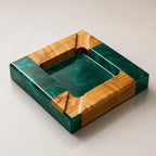 A square ashtray featuring a combination of natural light brown wood and deep emerald green resin. The design includes four integrated notches on the corners, with the resin forming the central basin and two opposing sides.