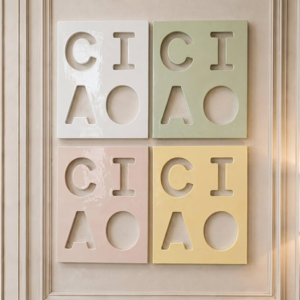Four rectangular wall tiles arranged in a grid, each featuring the cut-out letters C, I, A and a circle. The tiles are colored white, sage green, pale pink, and soft yellow, with a glossy finish and smooth, clean edges.