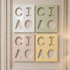 Four rectangular wall tiles arranged in a grid, each featuring the cut-out letters C, I, A and a circle. The tiles are colored white, sage green, pale pink, and soft yellow, with a glossy finish and smooth, clean edges.