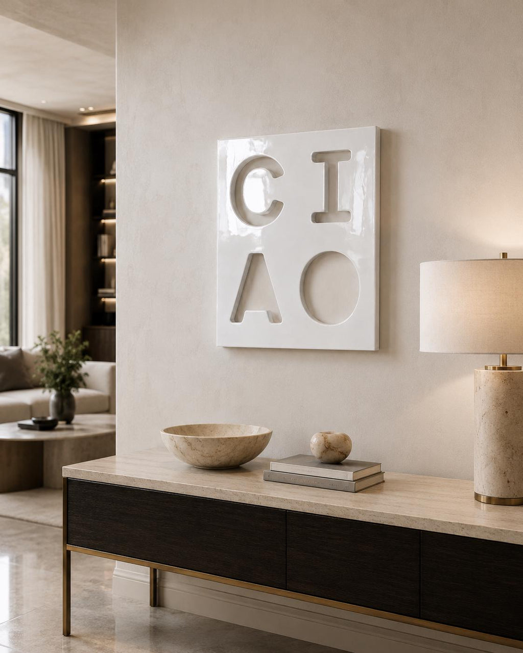A square white wall art piece featuring the word CIAO in large, recessed, cut-out letters. The artwork has a glossy finish and is mounted on a neutral-toned wall above a console table with a stone top and dark wood cabinet doors.