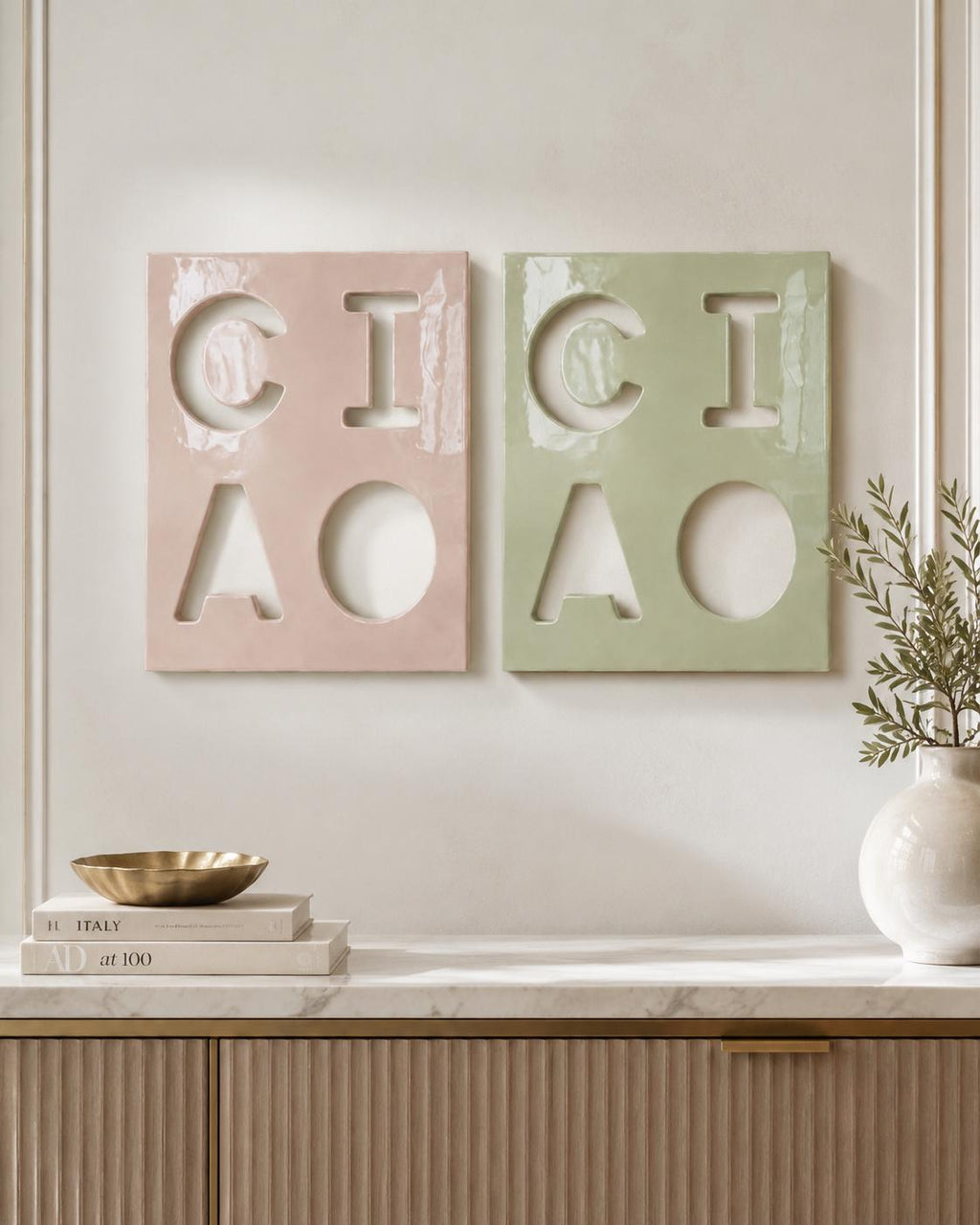 Two rectangular wall plaques featuring cut-out letters spelling CIAO. One plaque is a glossy pastel pink, and the other is a glossy sage green. Each plaque displays the letters C, I, A, and O arranged in a two-by-two grid pattern.