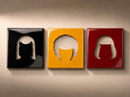 Three square wall plaques with a glossy finish. The left plaque is black with a cutout of a bob hairstyle. The center plaque is yellow with a cutout of an afro hairstyle. The right plaque is dark red with a cutout of a pageboy hairstyle.