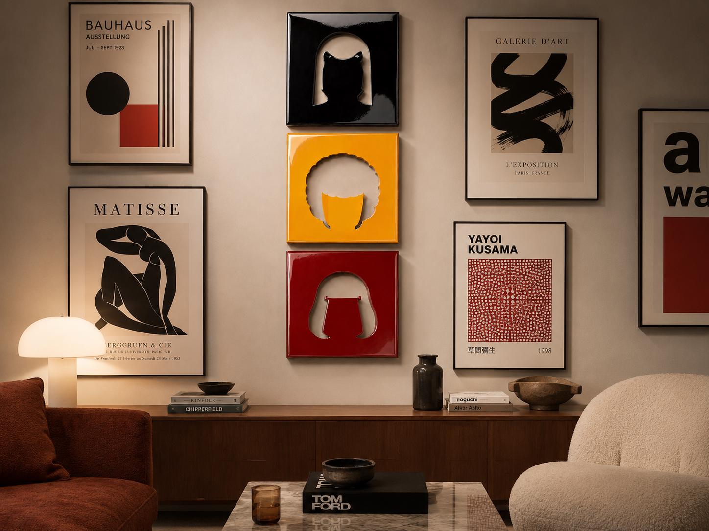 A gallery wall featuring a Bauhaus poster, a Matisse print, a Yayoi Kusama exhibition poster, and three square, glossy, cut-out wall panels in black, yellow, and red, arranged vertically between framed art prints on a neutral wall.