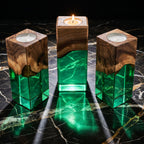 Three rectangular candle holders made of natural wood and translucent green resin. Each holder features a dark wood top with a live edge transition into a clear green base, with a circular white tea light candle inserted at the top.