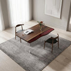A rectangular dining table with a dark brown wood top featuring a wavy red resin inlay, supported by clear acrylic legs. Two wooden chairs with black upholstered seats are positioned at the table, which holds an open book.