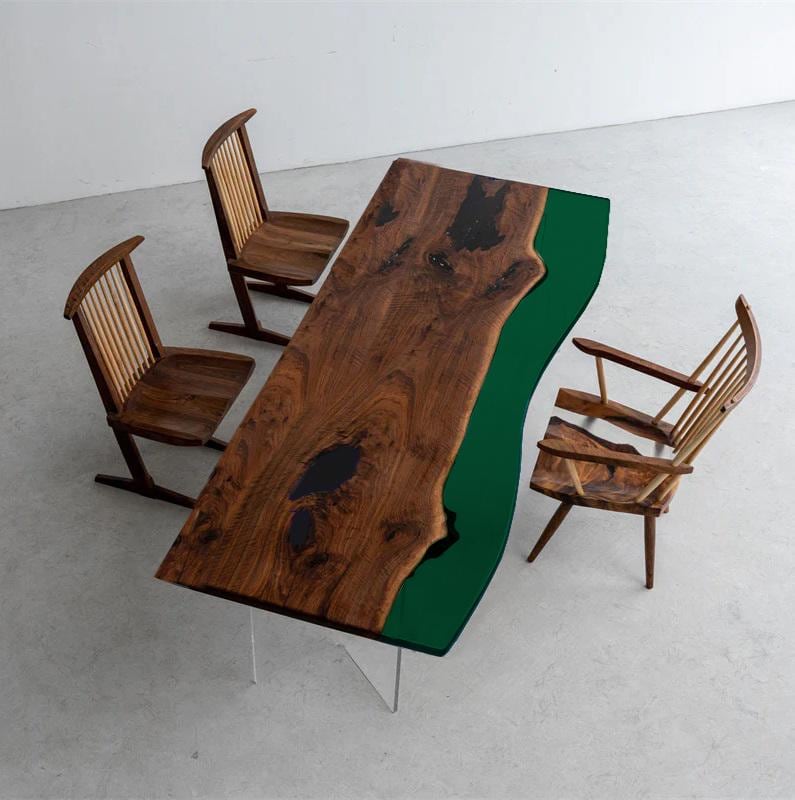 A rectangular dining table featuring a natural live-edge walnut wood slab with dark resin inlays and a solid deep green resin side section, supported by clear acrylic legs, accompanied by three wooden spindle-back chairs.