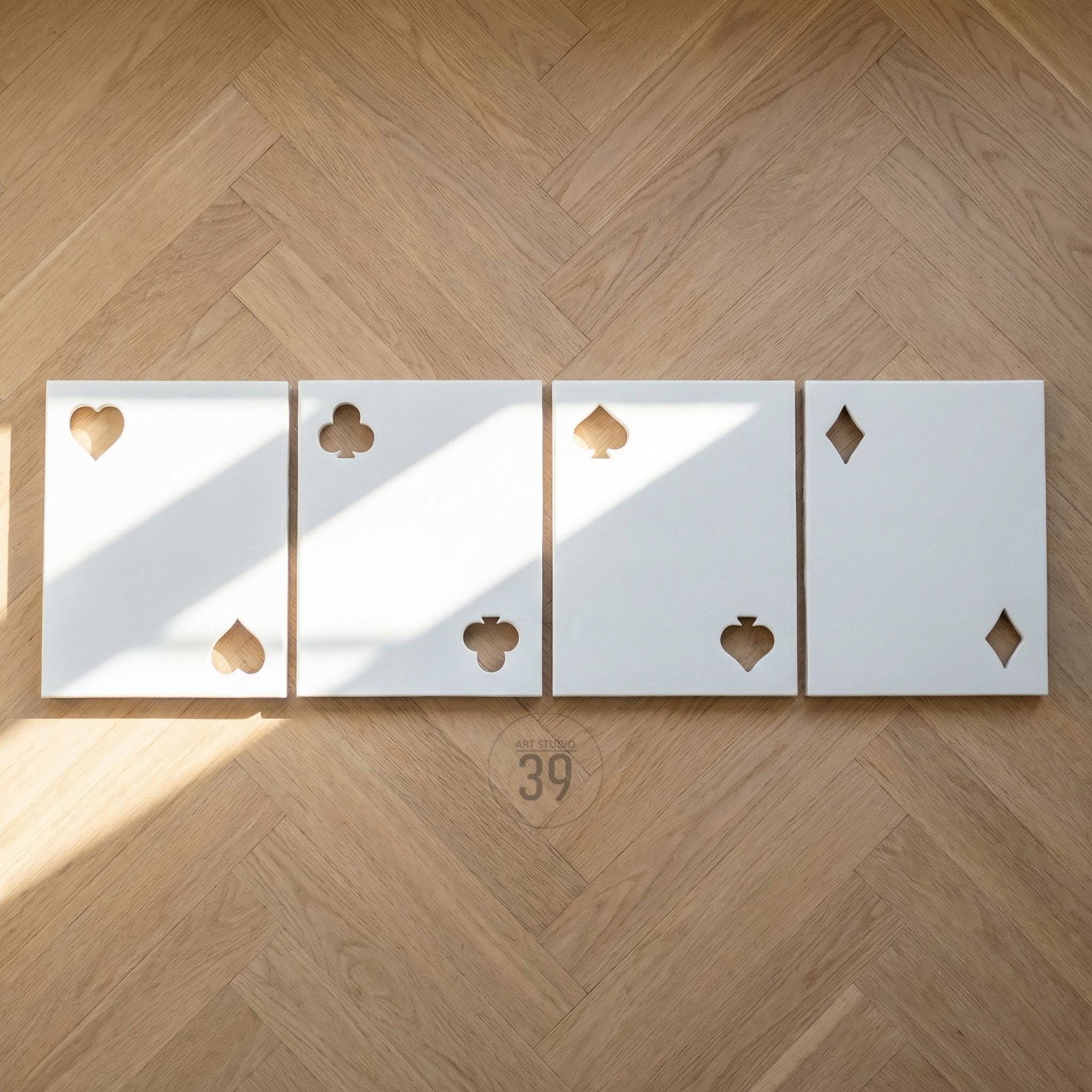 Four rectangular white panels arranged in a row, each featuring two cut-out shapes representing playing card suits. The first panel shows a heart and a spade, the second a club and a club, the third a spade and a spade, and the fourth a diamond and a diamond.