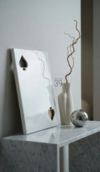 A white rectangular panel featuring two spade cutouts, a matte off-white vase containing a single twisted branch, and a polished silver sphere. The panel displays the text ART STUDIO 39 in a circular emblem on its surface.