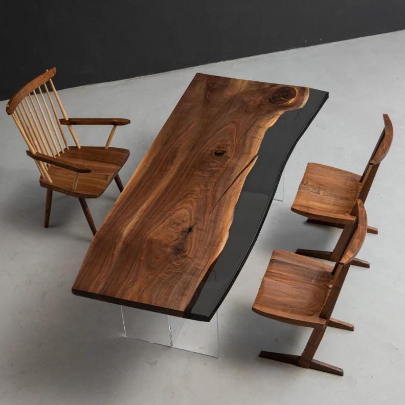 A dining set featuring a rectangular live-edge walnut wood table with a black resin inlay, supported by clear acrylic legs. The set includes one spindle-back wooden chair and two wooden chairs with angled legs and contoured seats.