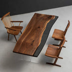 A dining set featuring a rectangular live-edge walnut wood table with a black resin inlay, supported by clear acrylic legs. The set includes one spindle-back wooden chair and two wooden chairs with angled legs and contoured seats.