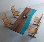 A rectangular dining table with a live-edge dark brown wood slab and a vibrant turquoise resin river inlay, supported by clear acrylic legs, accompanied by four light-toned wooden chairs with vertical slat backrests.