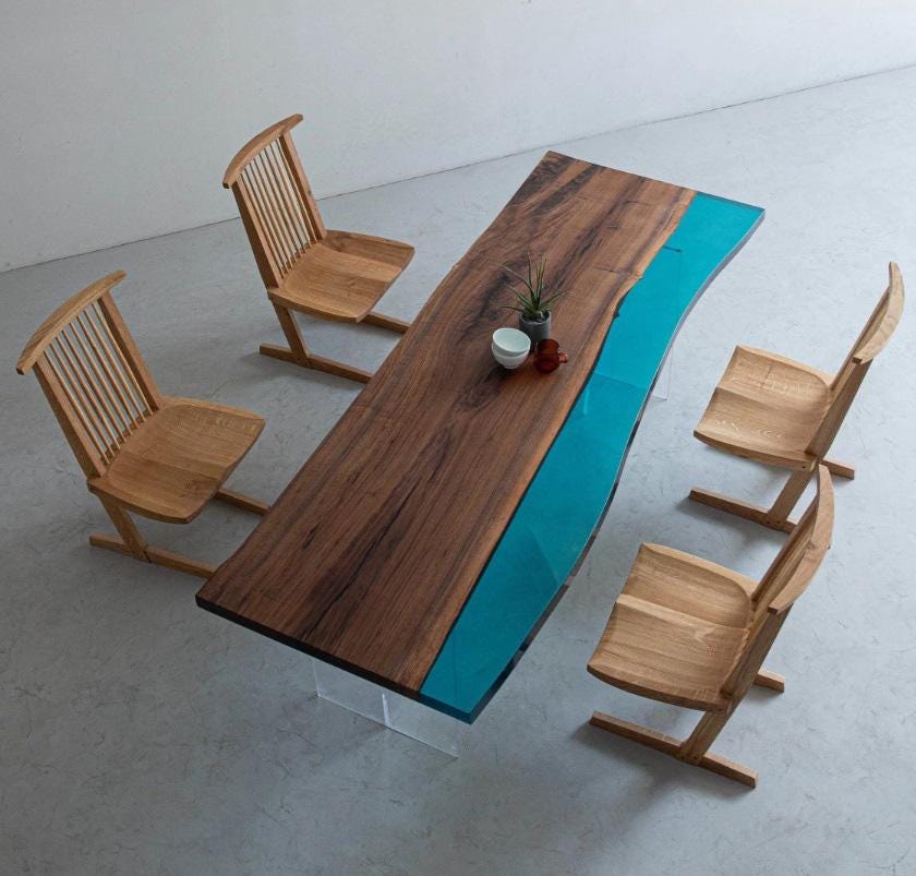 A rectangular dining table with a live-edge dark brown wood slab and a vibrant turquoise resin river inlay, supported by clear acrylic legs, accompanied by four light-toned wooden chairs with vertical slat backrests.
