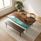 A rectangular dining table featuring a natural live-edge wood slab paired with a translucent teal resin section, supported by clear glass legs. The set includes a long wooden bench and two curved wooden chairs with black seats.