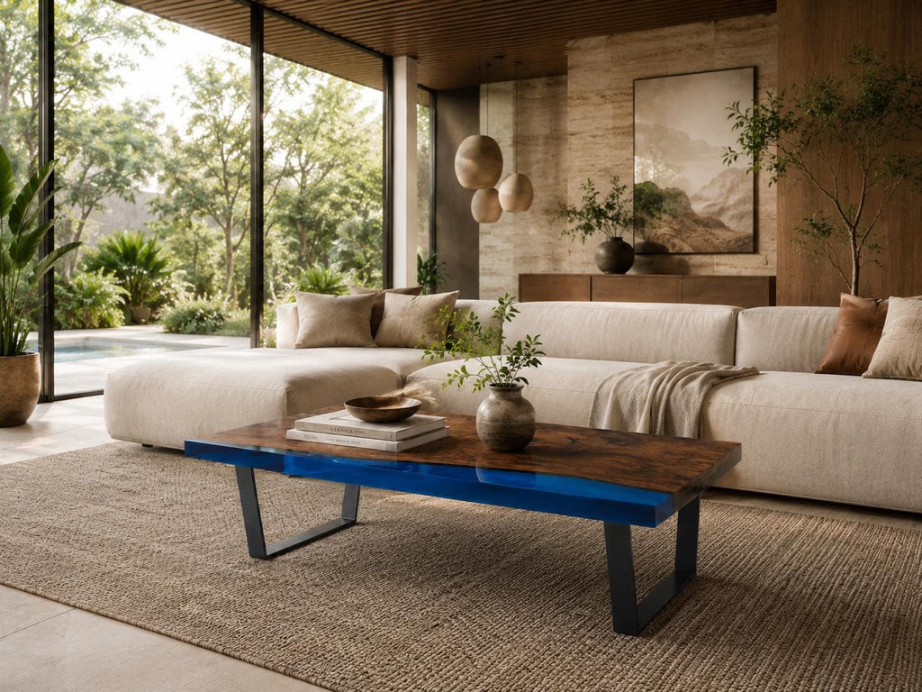 A rectangular coffee table featuring a natural wood grain surface with a vibrant blue resin inlay along the side, supported by black metal legs. The table holds a small ceramic bowl, a stack of books, and a small vase with greenery.