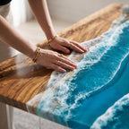 A rectangular table featuring a natural wood grain surface on one side and a vibrant blue resin inlay on the other. The resin section mimics ocean waves with white foam detailing, creating a smooth transition between the wood and water.