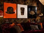 Three rectangular wall art panels featuring glossy finishes in orange, white, and black. The orange panel displays a bowler hat cutout, the white panel shows a trapezoidal cutout, and the black panel features a stylized eye design.