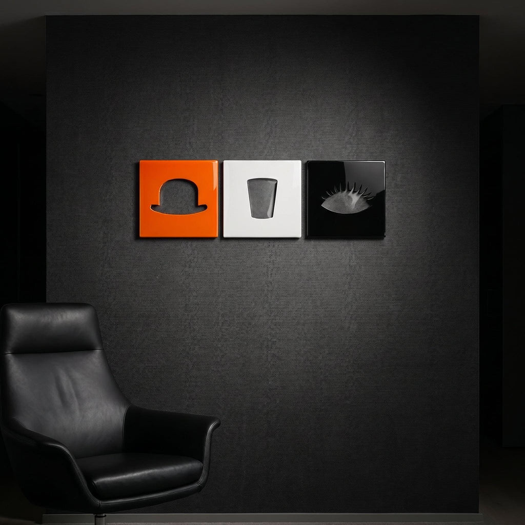 A set of three square wall art panels arranged horizontally. The left panel is orange with a black bowler hat silhouette, the center panel is white with a black glass silhouette, and the right panel is black with a white eye silhouette.
