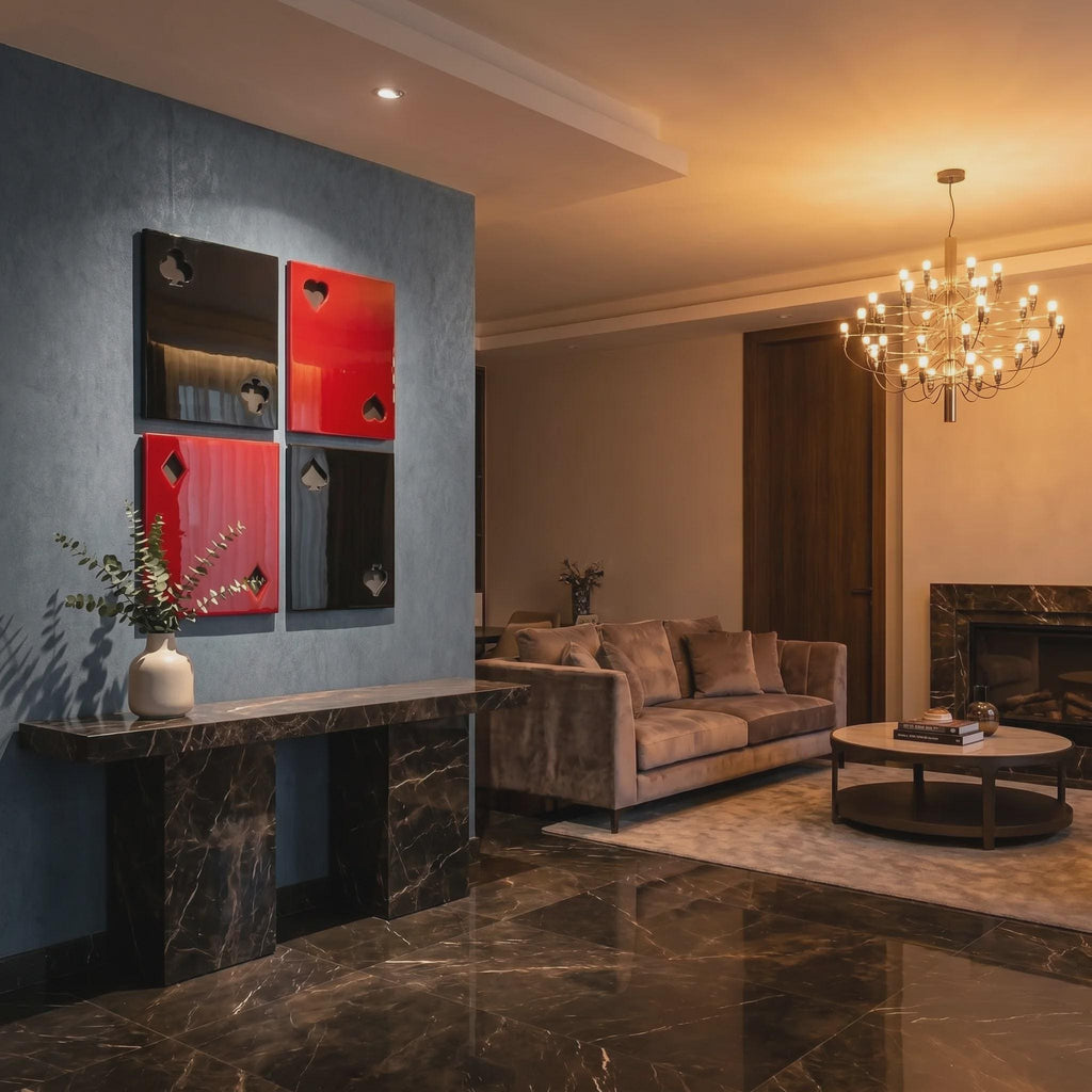Four square wall art panels arranged in a grid, featuring glossy black and red surfaces with cut-out playing card suit symbols including clubs, hearts, diamonds, and spades, mounted on a blue wall above a dark marble console table.