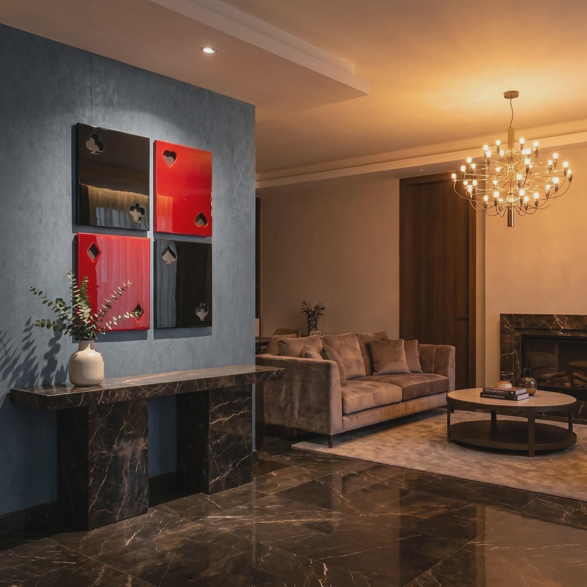 Four square wall art panels arranged in a grid, featuring glossy black and red surfaces with cut-out playing card suit symbols including clubs, hearts, diamonds, and spades, mounted on a blue wall above a dark marble console table.