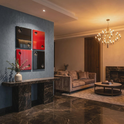Four square wall art panels arranged in a grid, featuring glossy black and red surfaces with cut-out playing card suit symbols including clubs, hearts, diamonds, and spades, mounted on a blue wall above a dark marble console table.