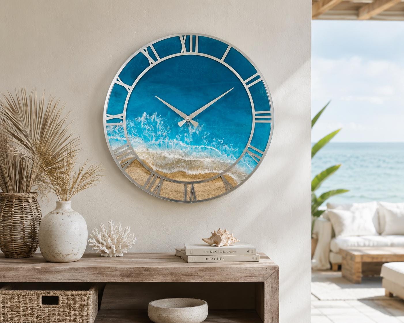 A round wall clock featuring a silver frame and Roman numerals. The clock face displays a detailed resin art depiction of a sandy beach meeting turquoise ocean waves with white sea foam, complemented by two slender silver clock hands.