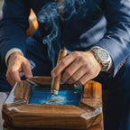A square wooden ashtray featuring a deep blue resin center with a small metallic whale figure embedded inside. The ashtray has a polished natural wood frame with angled corners and a smooth finish, designed for holding a lit cigar.