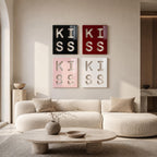 Four square wall art panels arranged in a grid, each featuring the word KISS in a cutout style. The top left panel is black, the top right is red, the bottom left is light pink, and the bottom right is white, all with glossy finishes.