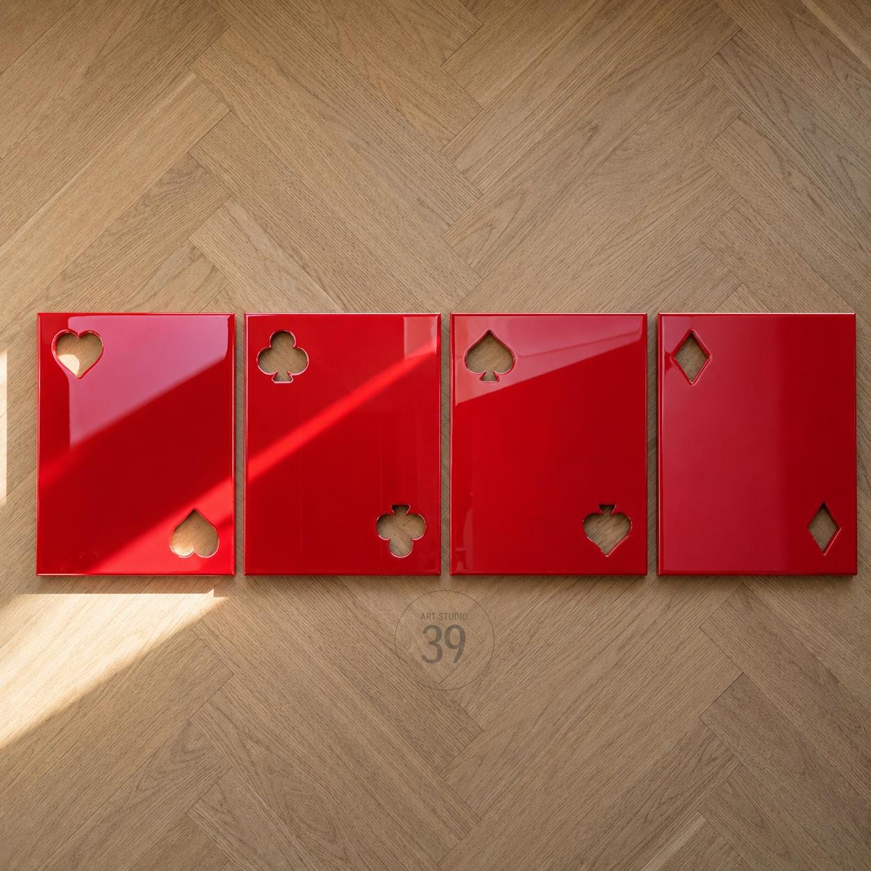 Four rectangular red panels arranged in a row, each featuring cutouts of playing card suits. The first panel has hearts, the second has clubs, the third has spades, and the fourth has diamonds. Each panel has a glossy, reflective finish.