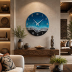 A circular wall clock featuring a resin art design that mimics an ocean shoreline with deep blue water, turquoise waves, white sea foam, and a black sand beach. The clock face displays white Roman numerals and two white clock hands.